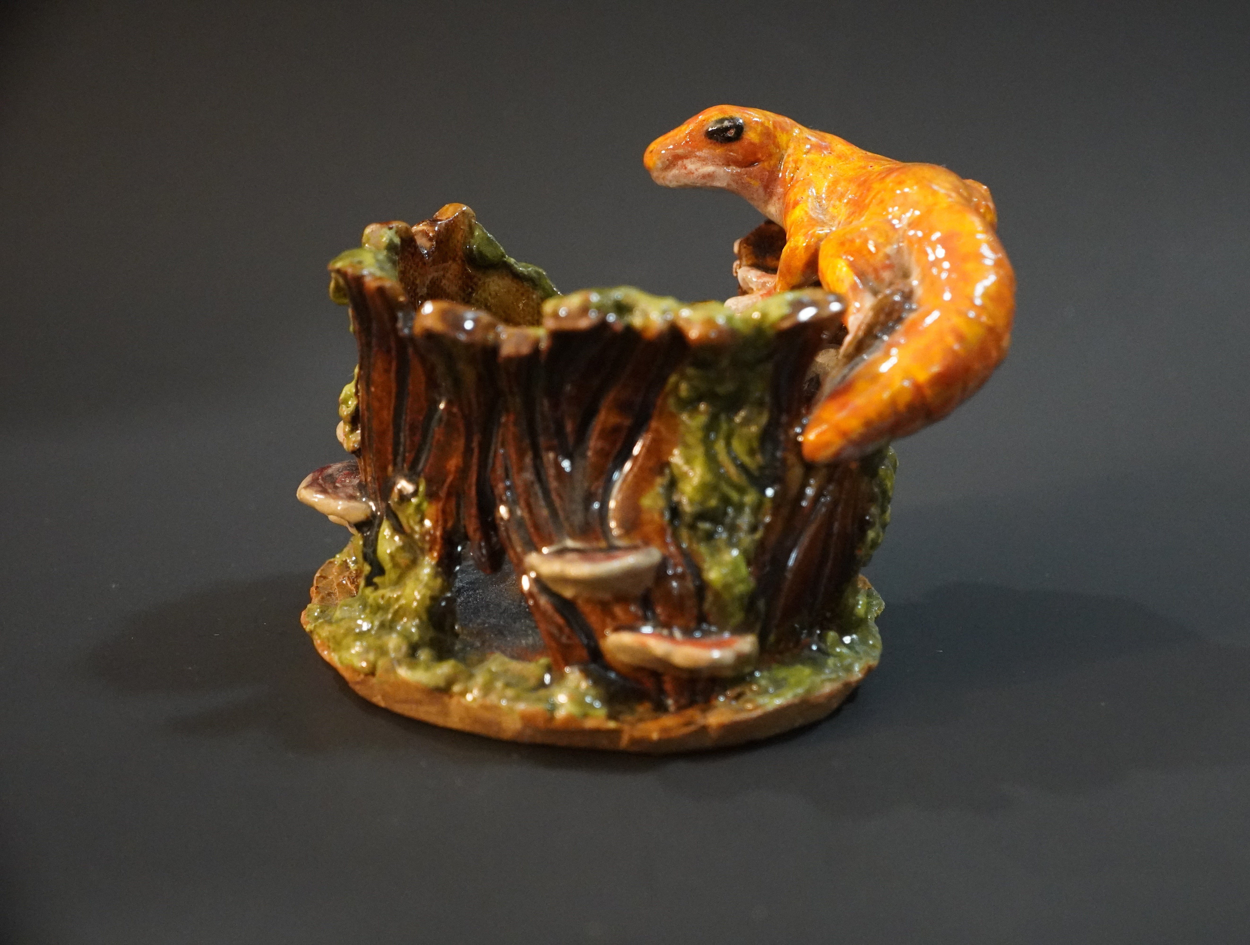 Ceramic sculpture of an orange gecko on a stump, covered in moss and mushrooms
