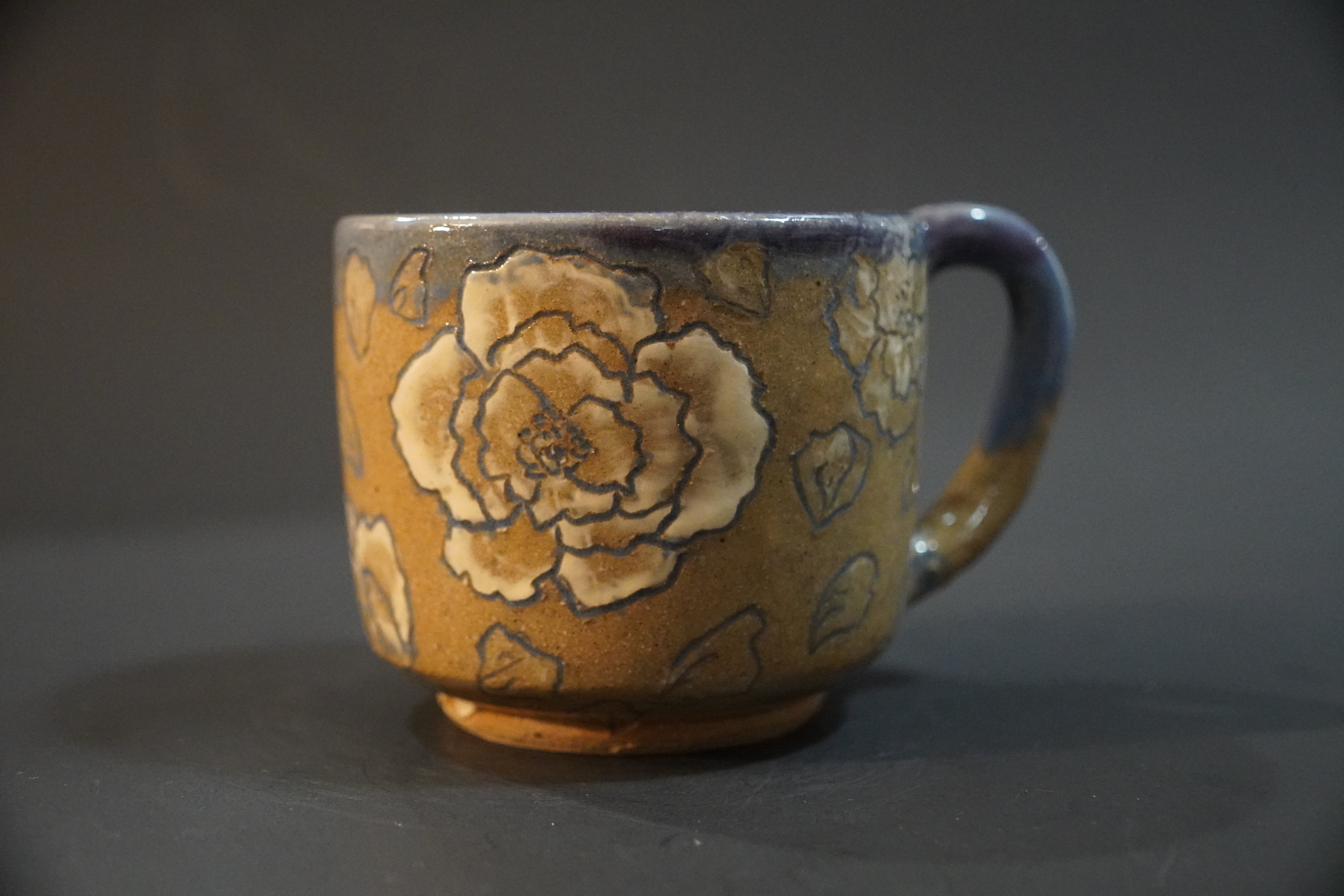 Ceramic mug with white flowers painted and carved into it, lined with purple